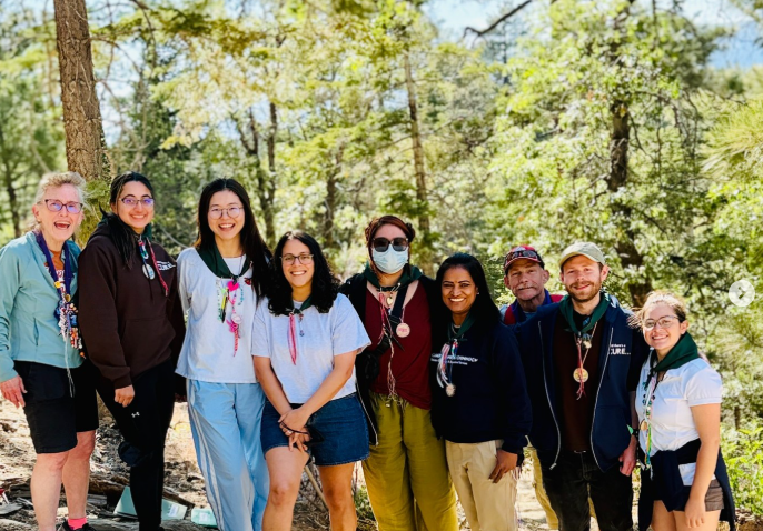 pharmacy students and faculty group standing outside among tall pine trees and blue skies