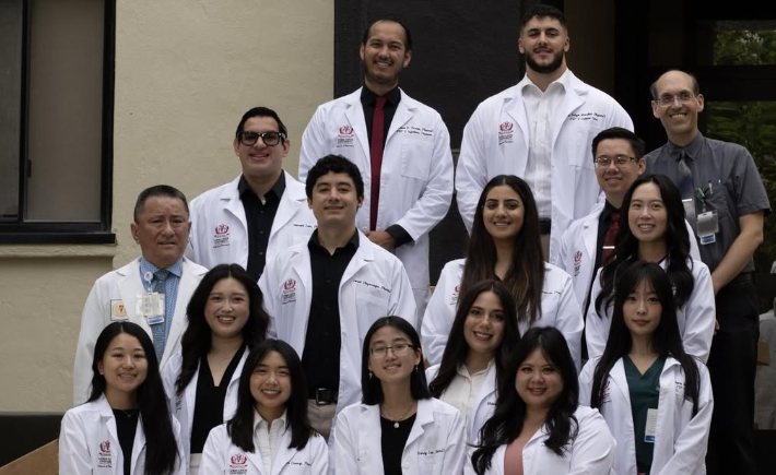 New and returning pharmacy residents in lab coats standing outside on the steps of the Shryock Hall building entrance