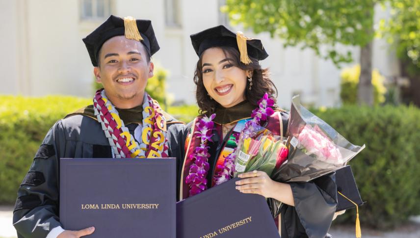 Graduates in regalia holding diplomas smiling