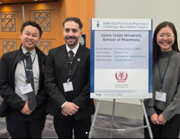 Three Students pose in front of the quarterfinal team challenge poster