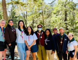 pharmacy students and faculty group standing outside among tall pine trees and blue skies