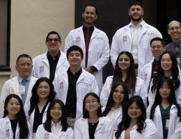 New and returning pharmacy residents in lab coats standing outside on the steps of the Shryock Hall building entrance